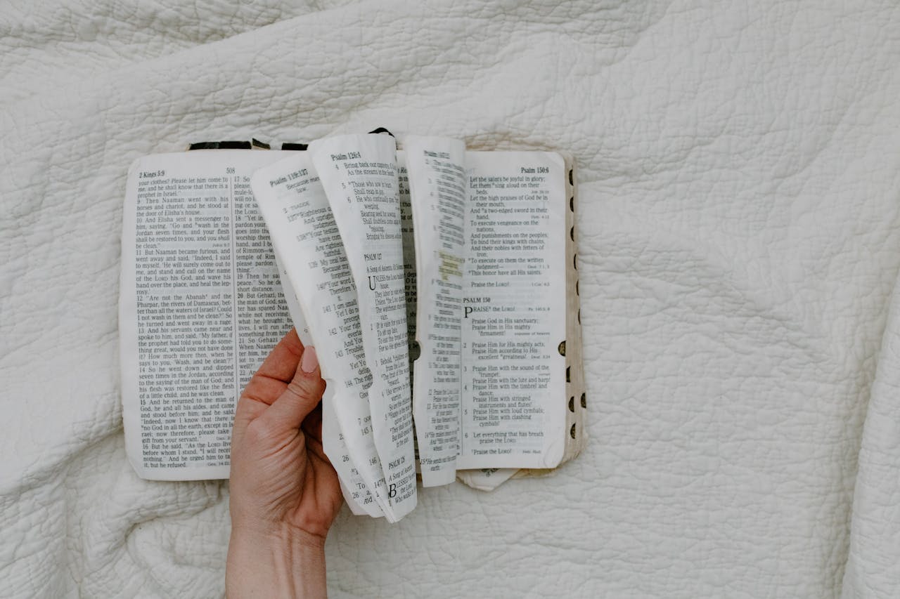 services-03 A hand gently holds an open Bible, showcasing its pages on a white fabric background.